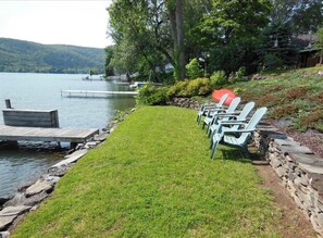 Relax in a serene lakeside setting with Adirondack chairs and a wooden dock.
