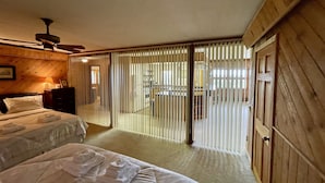 Une chambre d’hôtel avec deux lits, un ventilateur de plafond, des murs en bois, une porte coulissante et une vue sur la cuisine.