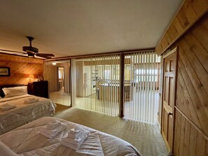 Camera d'albergo con due letti, una ventola a soffitto, pareti in legno, una porta scorrevole e vista sull'area cucina.