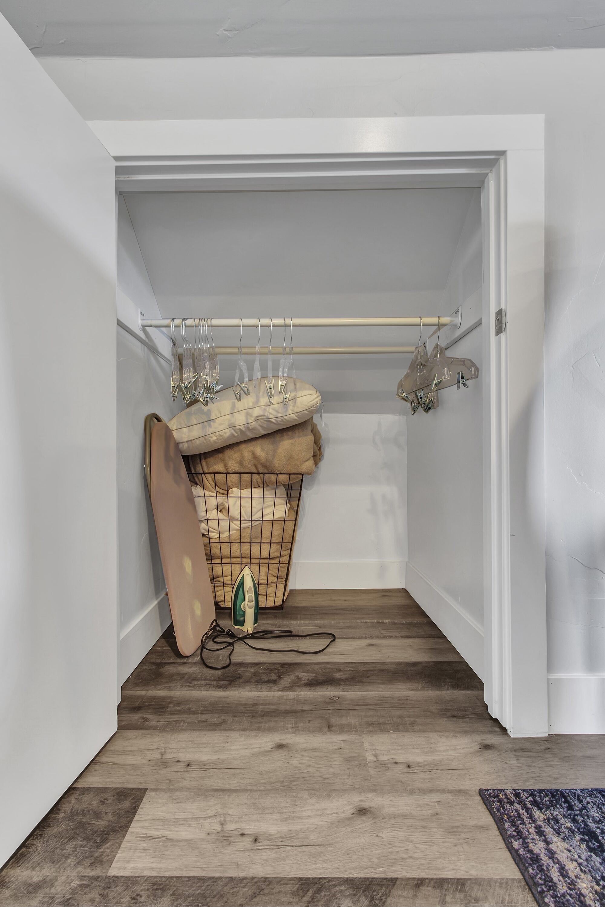 A compact room with a wooden floor, a hanging clothes rack, and a small storage unit with a cushion.