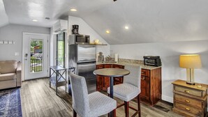 Cozinha compacta com geladeira, micro-ondas e torradeira. Há uma mesa de jantar com cadeiras, um armário de madeira e um abajur.