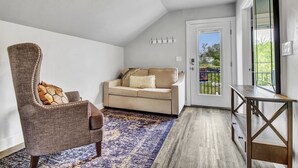 Sala de estar com teto alto, sofá bege, tapete estampado, cadeira de madeira e porta de vidro que dá para área externa.