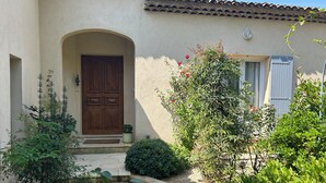 Un edificio con puerta de madera, un pequeño jardín con planta en maceta y tejado de tejas.