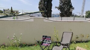 Un patio al aire libre con una mesa y cuatro sillas, rodeado por un muro bajo y follaje.
