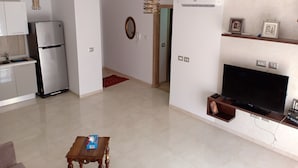 Una sala de estar moderna con televisión de pantalla plana, una zona de cocina con refrigerador y una mesa de comedor.