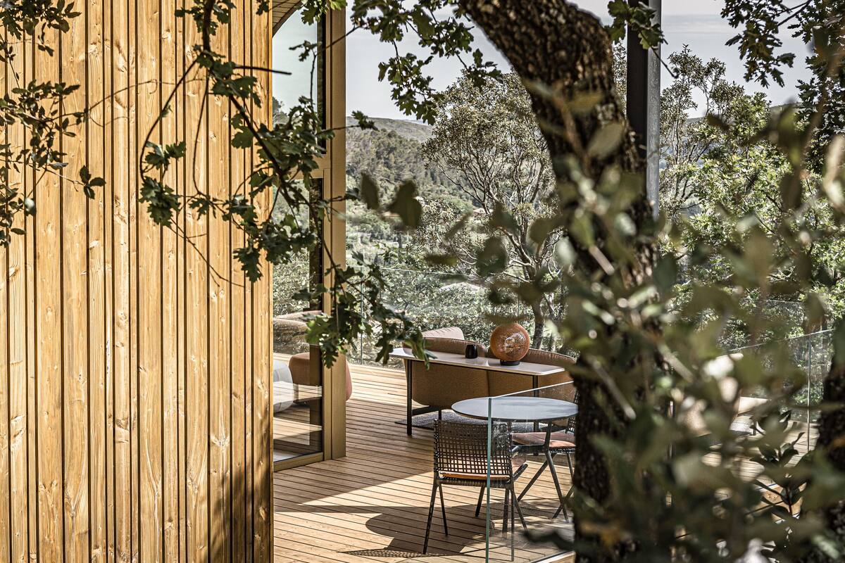 A wooden deck with outdoor furniture, including a sofa and a table, surrounded by trees.