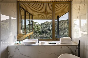 Un baño moderno con encimera de mármol, un lavabo redondo y un ventanal con vistas a un paisaje montañoso.
