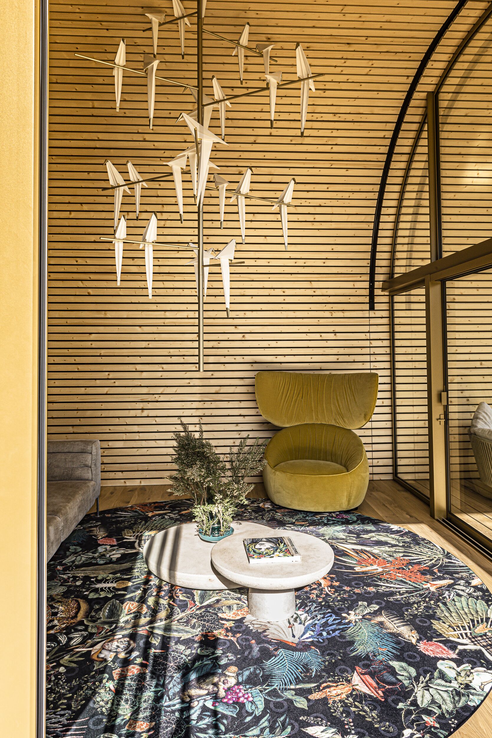 Una habitación con techo de listones de madera, una mesa redonda con un libro, una silla verde y una alfombra estampada.