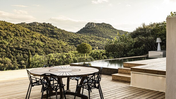 A wooden deck with a round table and chairs, overlooking a mountainous landscape and a body of water. - Souki Lodges & Spa (Cabrières)
