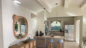 A modern kitchen with a large island, a built-in oven, and a refrigerator. There is a window providing natural light and a view of greenery outside.