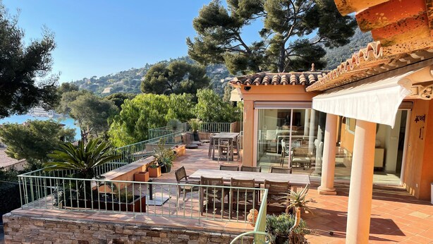 A terrace with outdoor seating, a stone wall, and a view of the sea.
