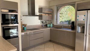 A modern kitchen with stainless steel appliances, a window with a view of greenery, and a water dispenser.