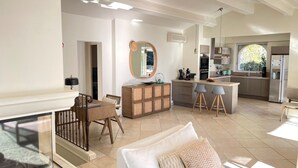 A spacious living area with a dining table, sofa, and a kitchen area with a bar.