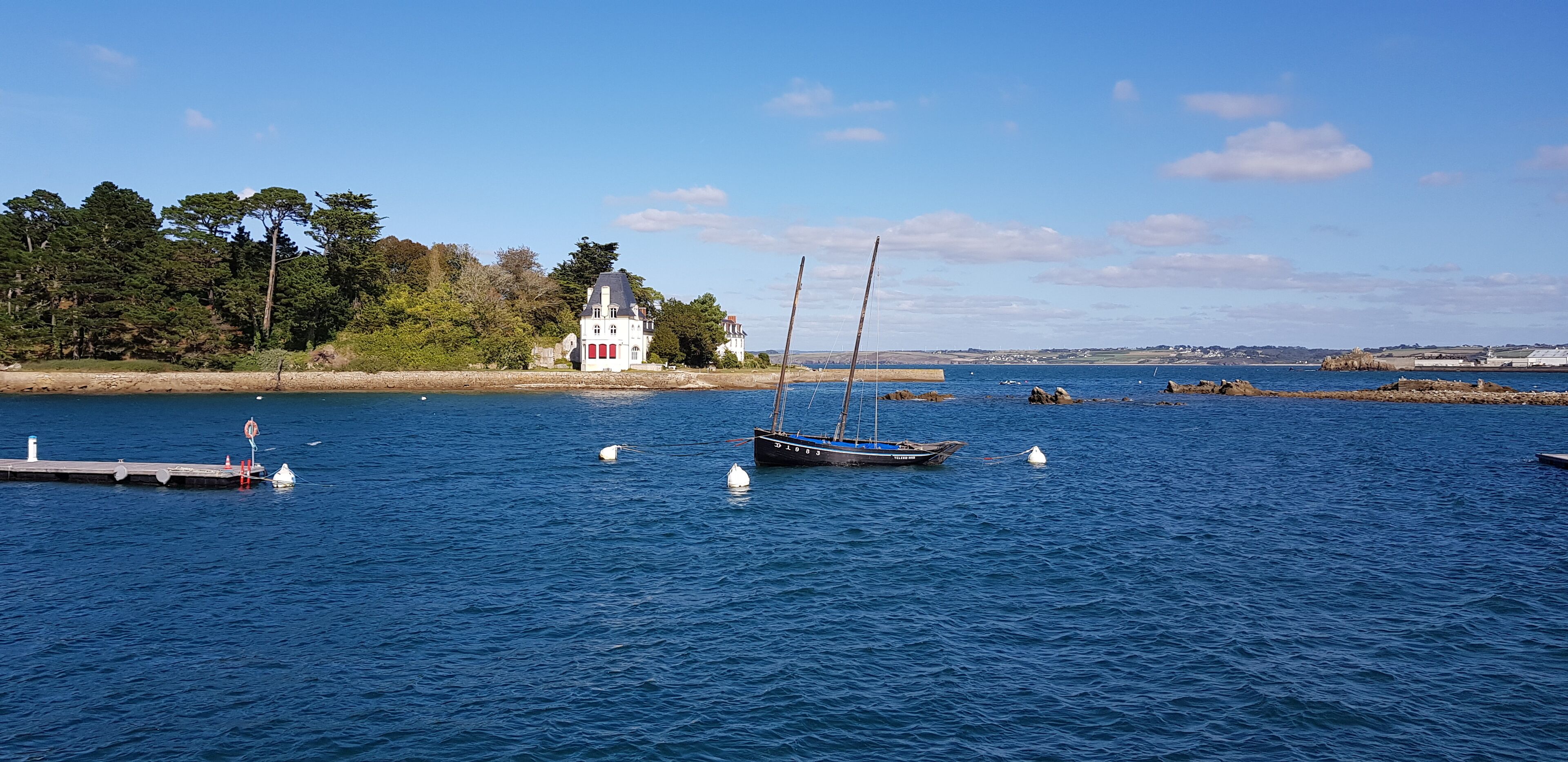 A coastal scene with a white building, a dock, and several boats on calm waters.