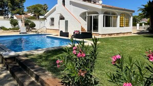 A white villa with a swimming pool, a well-maintained lawn, and a clear blue sky.