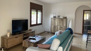 A living room with a TV, sofa, coffee table, and a window with blinds.