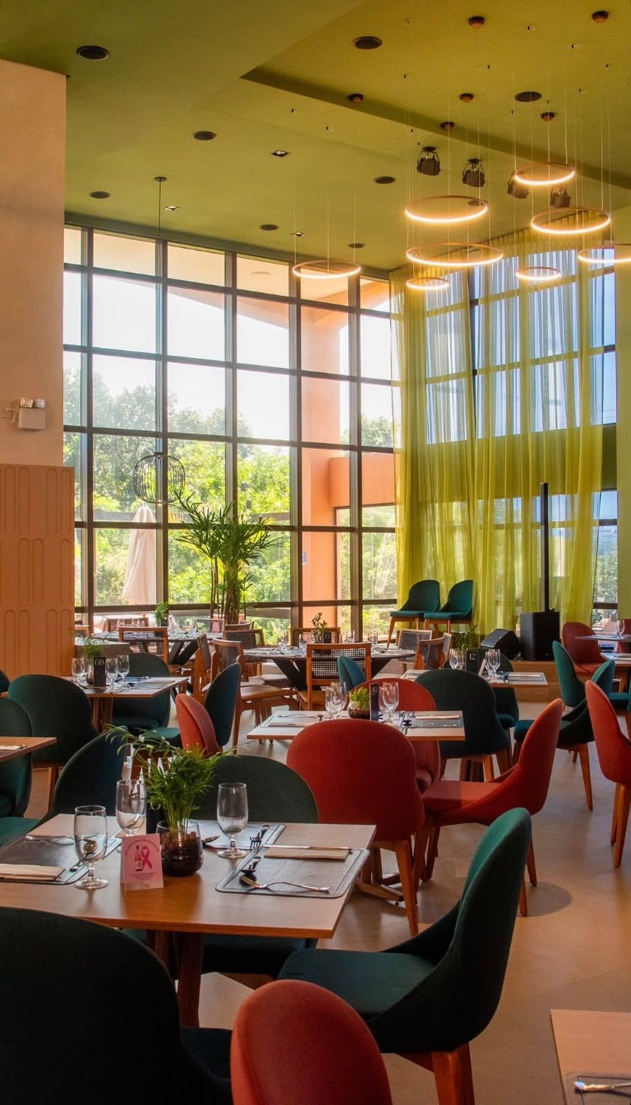 Un restaurante con varias mesas y sillas, ventanas amplias y lámparas colgantes.