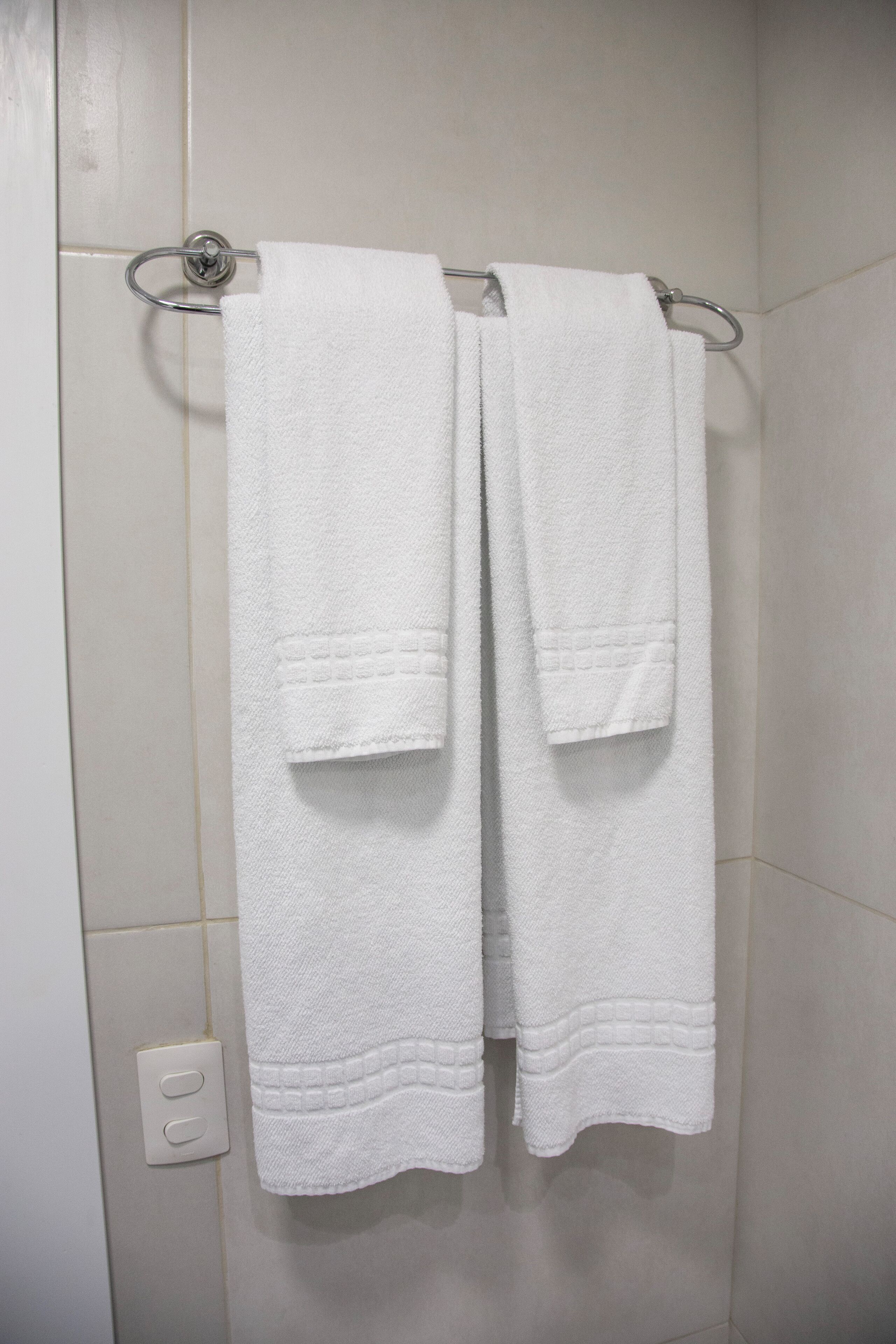 A bathroom with white tiled walls and a towel rack holding two white towels.