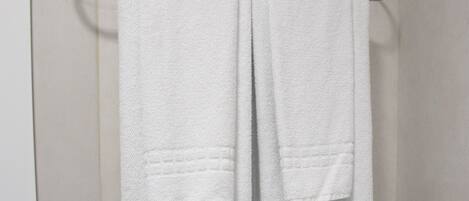 A bathroom with white tiled walls and a towel rack holding two white towels.