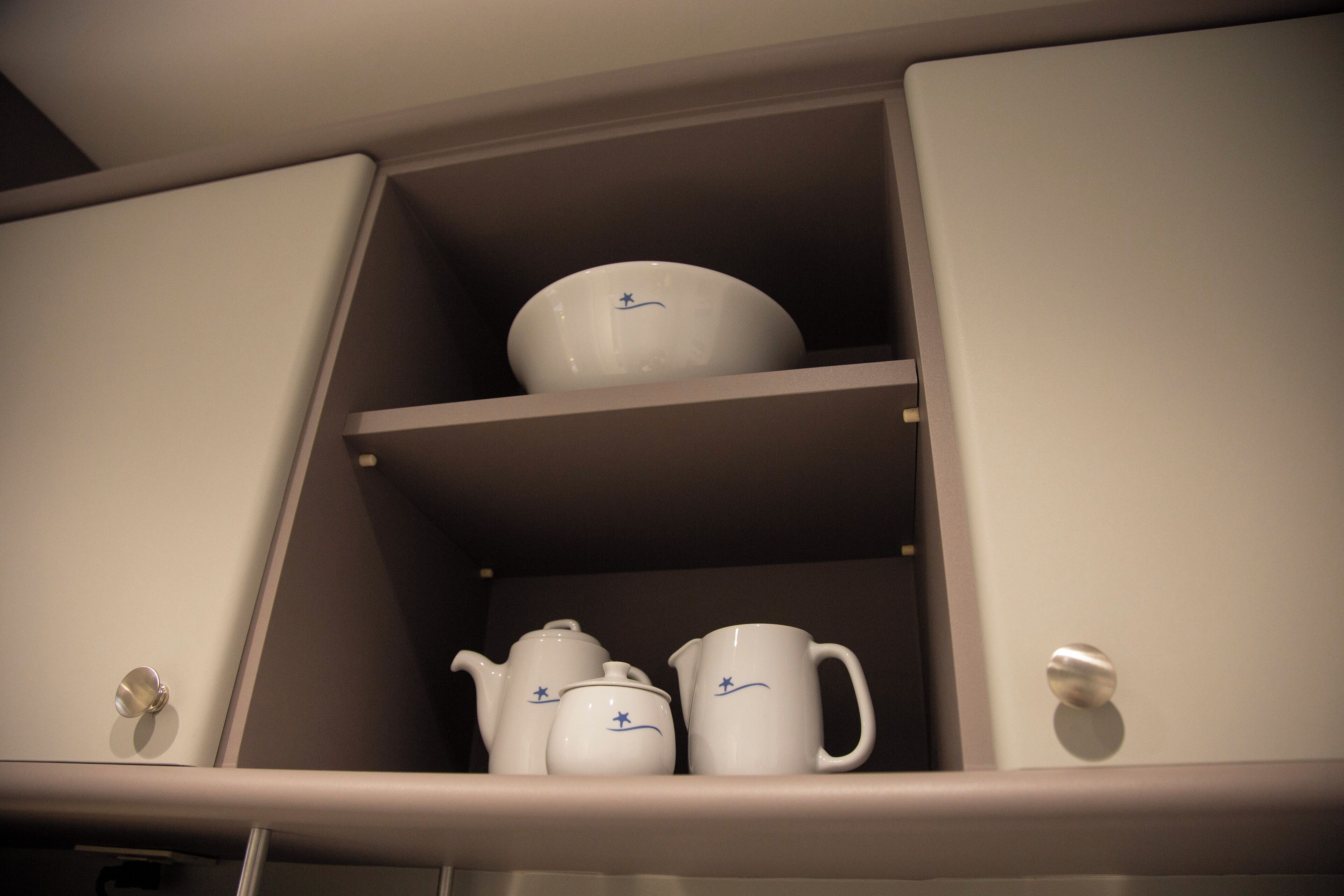 A cabinet with three white ceramic items: a teapot, a cup, and a bowl.