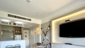 A modern kitchen with a dining area, white cabinetry, and a flat-screen TV mounted on the wall. - Jurerê Beach Village (Florianópolis)
