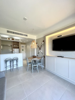 A modern kitchen with a dining area, white cabinetry, and a flat-screen TV mounted on the wall. - Jurerê Beach Village (Florianópolis)