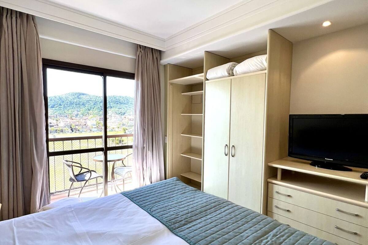 A hotel room with a large bed, a TV, a wardrobe, and a balcony with a view.