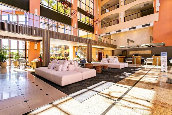 A spacious lobby with a high ceiling, a central seating area with sofas, and a staircase leading to upper floors. - Jurerê Beach Village (Florianópolis)