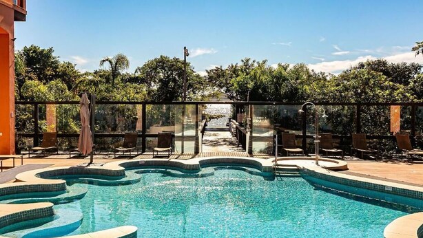 Une piscine à bords ondulés, entourée de chaises longues et protégée par une paroi de verre.
