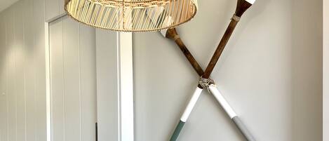 A dining area with a round wooden table, blue chairs, a woven rattan pendant light, and two wooden-handled paintbrushes mounted on the wall.