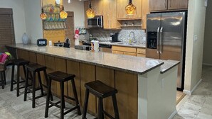 A modern kitchen with wooden cabinets, a stainless steel refrigerator, a microwave, and a bar area with stools. - 🌊 Private Oasis With Pool Spa Dock and Ocean right in your backyard 🌊 allow pets (Marathon)