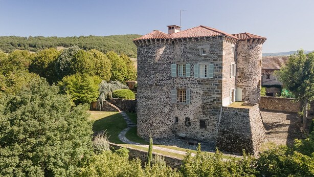 A stone tower with a red-tiled roof, surrounded by lush greenery and a clear sky. - A luxurious chateau in the Auvergne in a remarkable setting! (Cerzat)