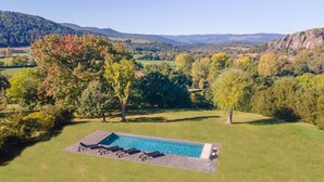An aerial view of a property with a swimming pool, surrounded by lush greenery and hills. - A luxurious chateau in the Auvergne in a remarkable setting! (Cerzat)