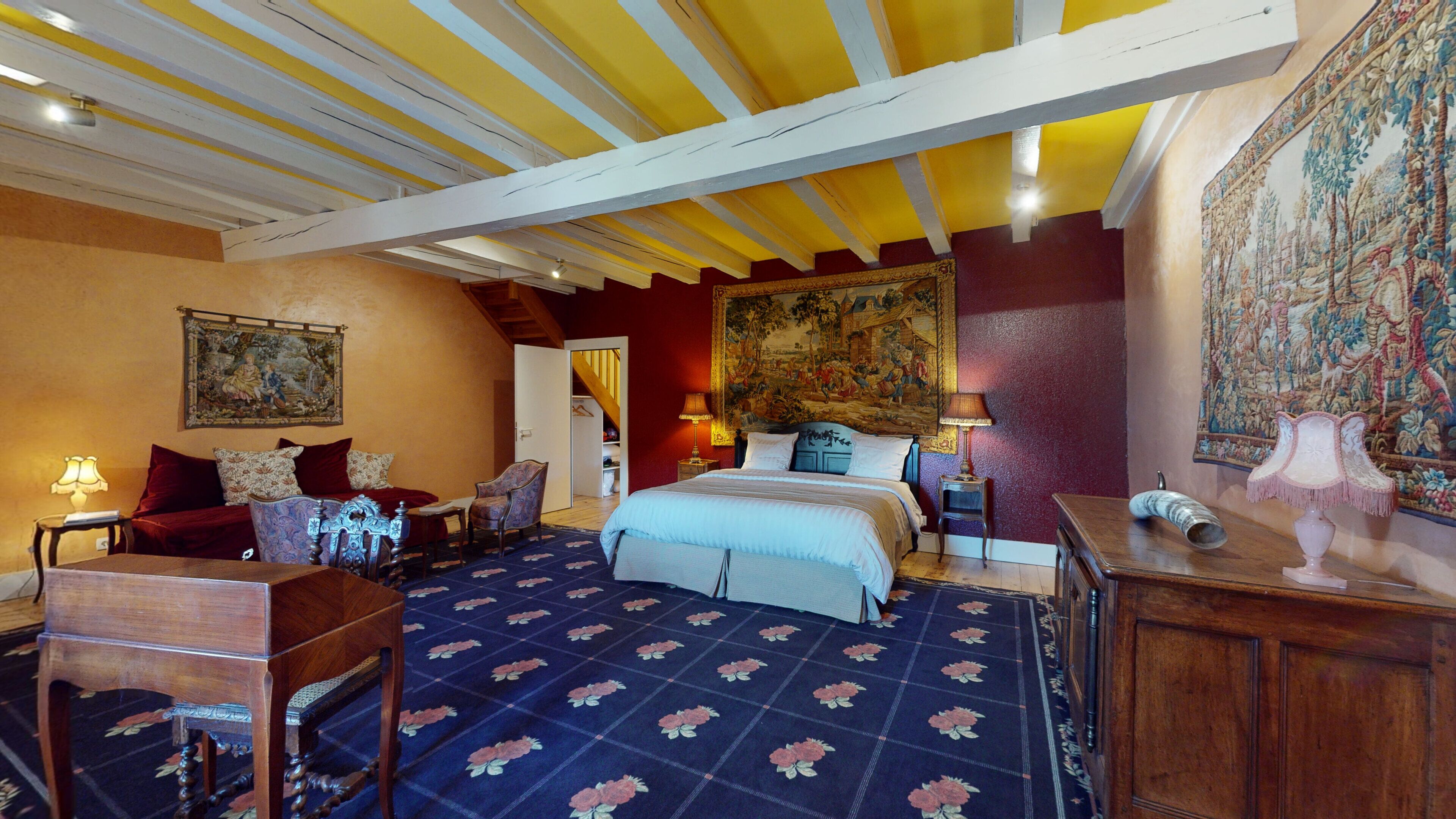 A bedroom with a large bed, a chair, a desk, and a tapestry on the wall.