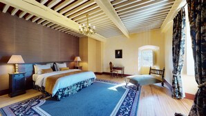 A hotel room with a large bed, two bedside tables, a desk, a chair, a chandelier, and a window with curtains. - A luxurious chateau in the Auvergne in a remarkable setting! (Cerzat)