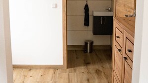 A narrow hallway with a wooden floor leading to a kitchen area with a sink and cabinets. - Apartment at the Alpakahof (Kleinnondorf)