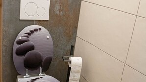 A modern bathroom with a unique toilet design, a toilet paper holder, and a visible water heater. - Apartment at the Alpakahof (Kleinnondorf)