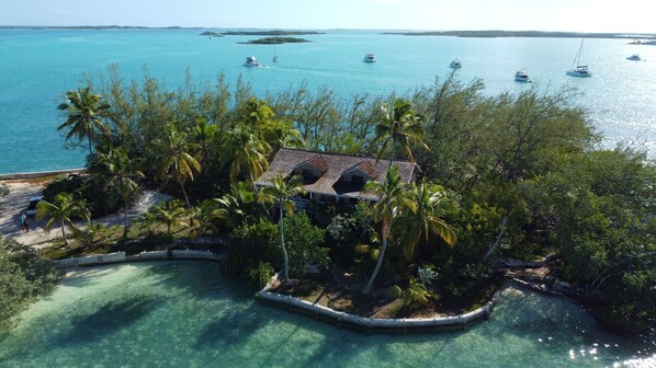 A tropical resort with a clear view of the ocean, palm trees, and a small building surrounded by a pool.