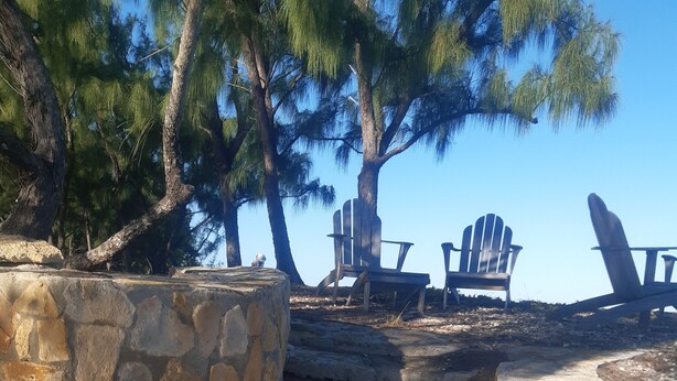 A stone pathway leading to a seating area with Adirondack chairs, surrounded by trees. - Private Island w Causeway to Town, 2 Bedroom, 2 bathroom, Full kitchen, Sleeps 6 (George Town)
