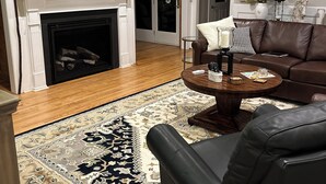 A living room with a fireplace, a television, a ceiling fan, a brown leather sofa, and a patterned rug. - Executive Home Gated Golf Community close to Masters! (Aiken)
