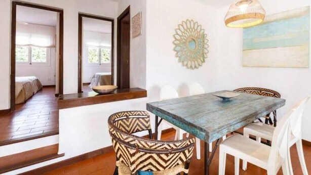 Un comedor con una mesa de madera y sillas estampadas, un adorno en la pared, y vistas a otra habitación.