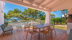 Un patio techado con una mesa y sillas, una piscina al fondo y vista al mar.