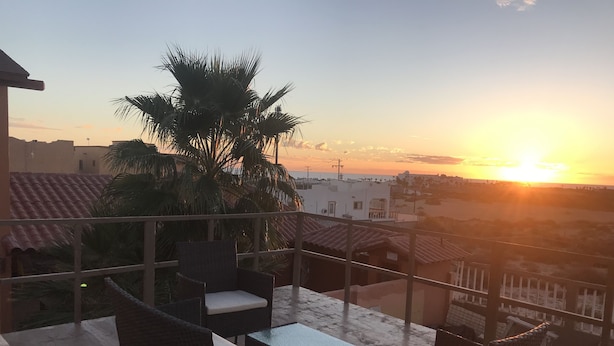 A balcony with wicker furniture, a view of the sunset, and palm trees. - loft morado (Puerto Peñasco)