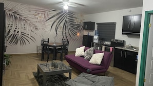 A living room with a sofa, coffee table, and chairs. There is a kitchen area with cabinets and a refrigerator. - loft morado (Puerto Peñasco)