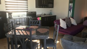 A modern kitchen with dark cabinets, a dining table with chairs, and a purple sofa with cushions. - loft morado (Puerto Peñasco)