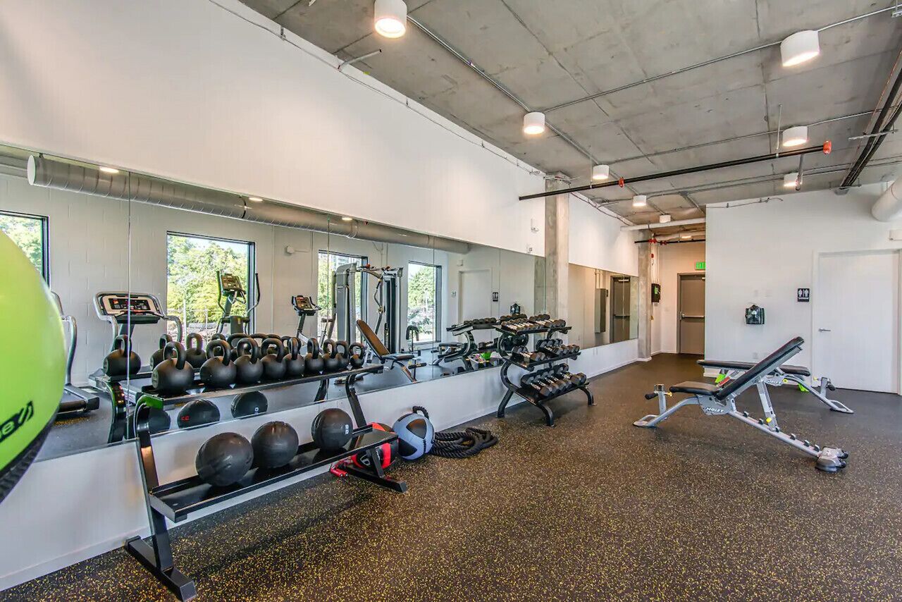 Un gimnasio con equipo de ejercicio, un espejo grande y una ventana que da a vistas de árboles.
