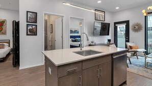 A modern kitchen with a central island, a built-in sink, and a flat-screen TV mounted above the island.