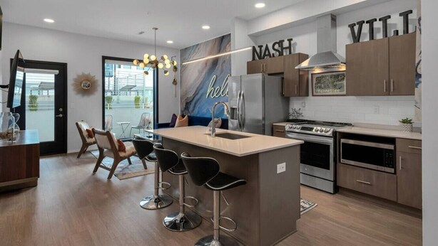 A modern kitchen with a central island, bar stools, a refrigerator, oven, microwave, and a wall-mounted sign with 'NASH' and 'VTT'.
