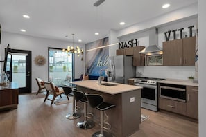 Una cocina moderna con una isla central, taburetes de bar, refrigerador, horno, microondas y un letrero en la pared que dice 'NASH' y 'VTT'.