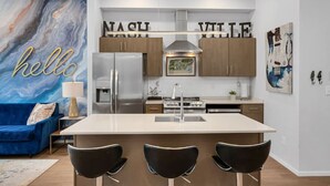 A modern kitchen with a central island, stainless steel appliances, and a blue sofa in the living area.